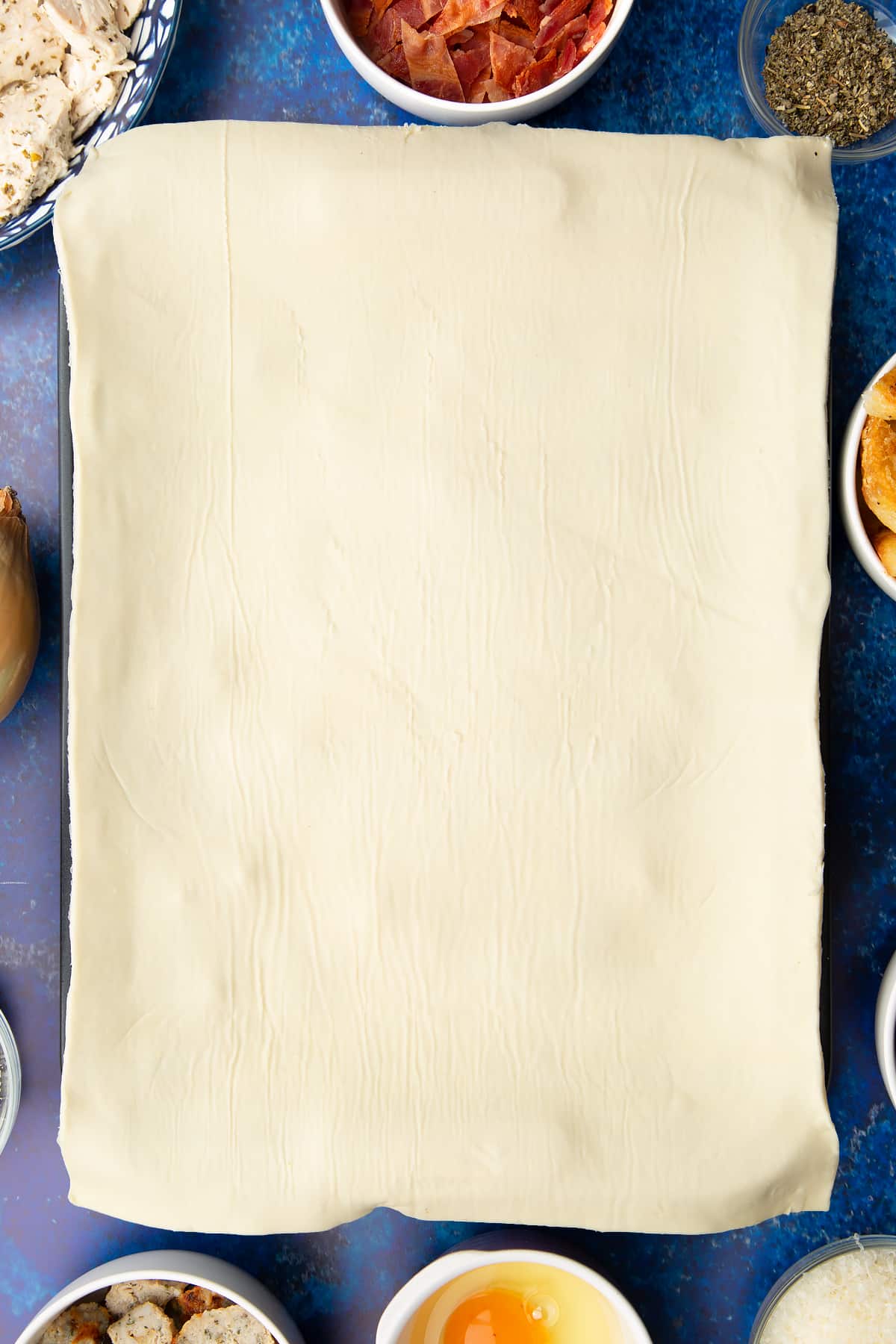 A roasting dish topped with a sheet of puff pastry. Ingredients to make a leftover Christmas dinner pie surround the tray.