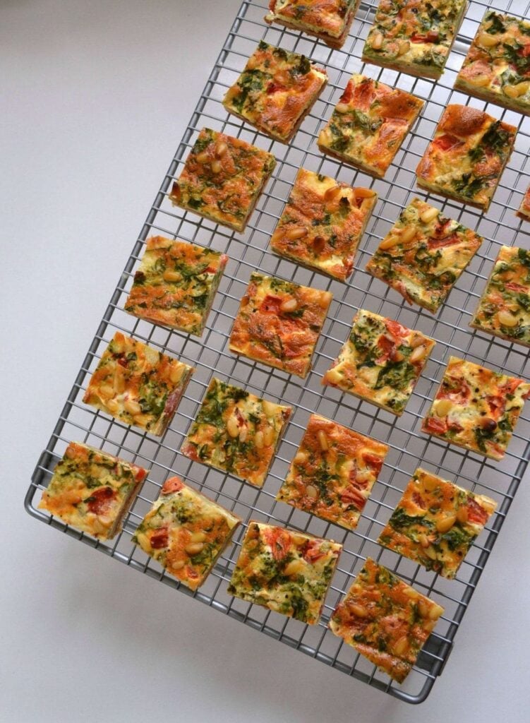 Mini quiche bites laid out in squares on a wire rack on a plain white background.