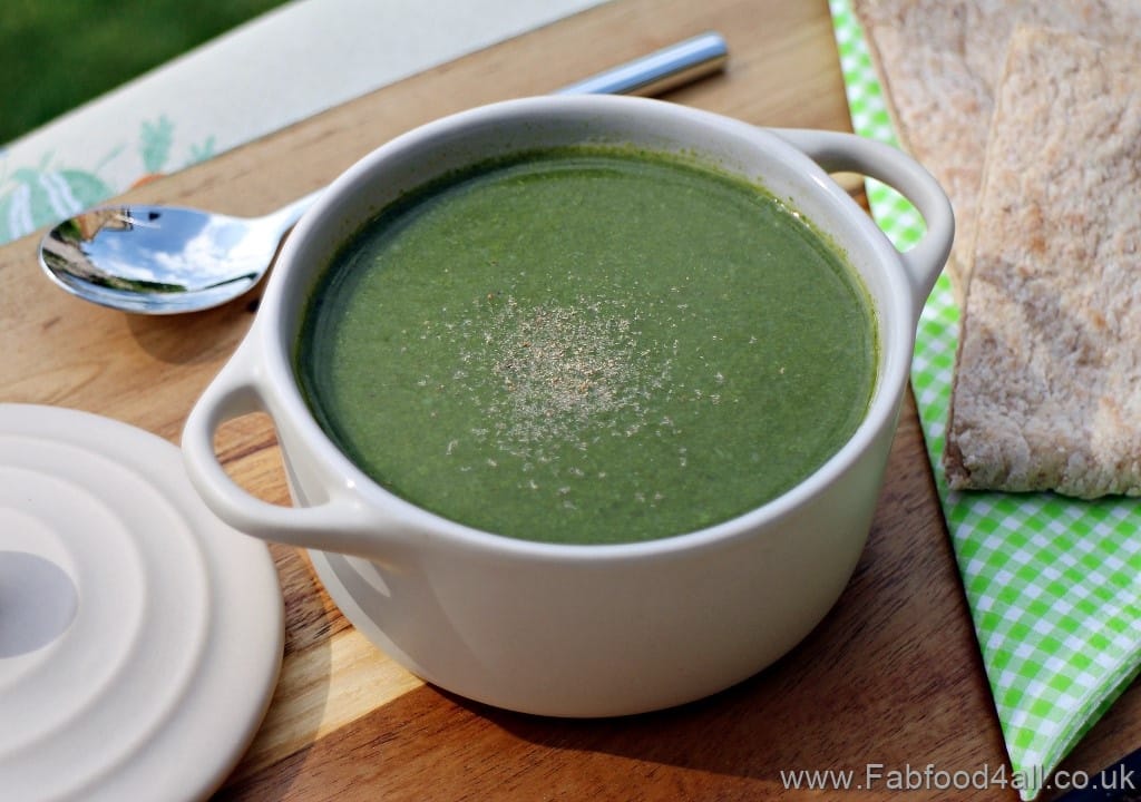 A white bowl with a handle on eitherside filled with spinach soup on a wooden board. 