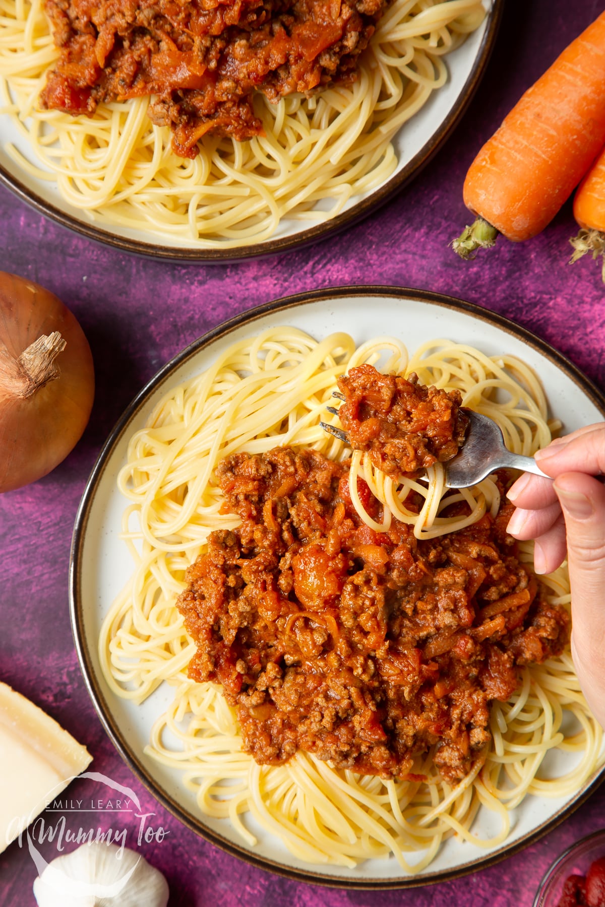 Close up of spaghetti bolognese Gordon Ramsay style served on plates. A fork lifts spaghetti from the plate.