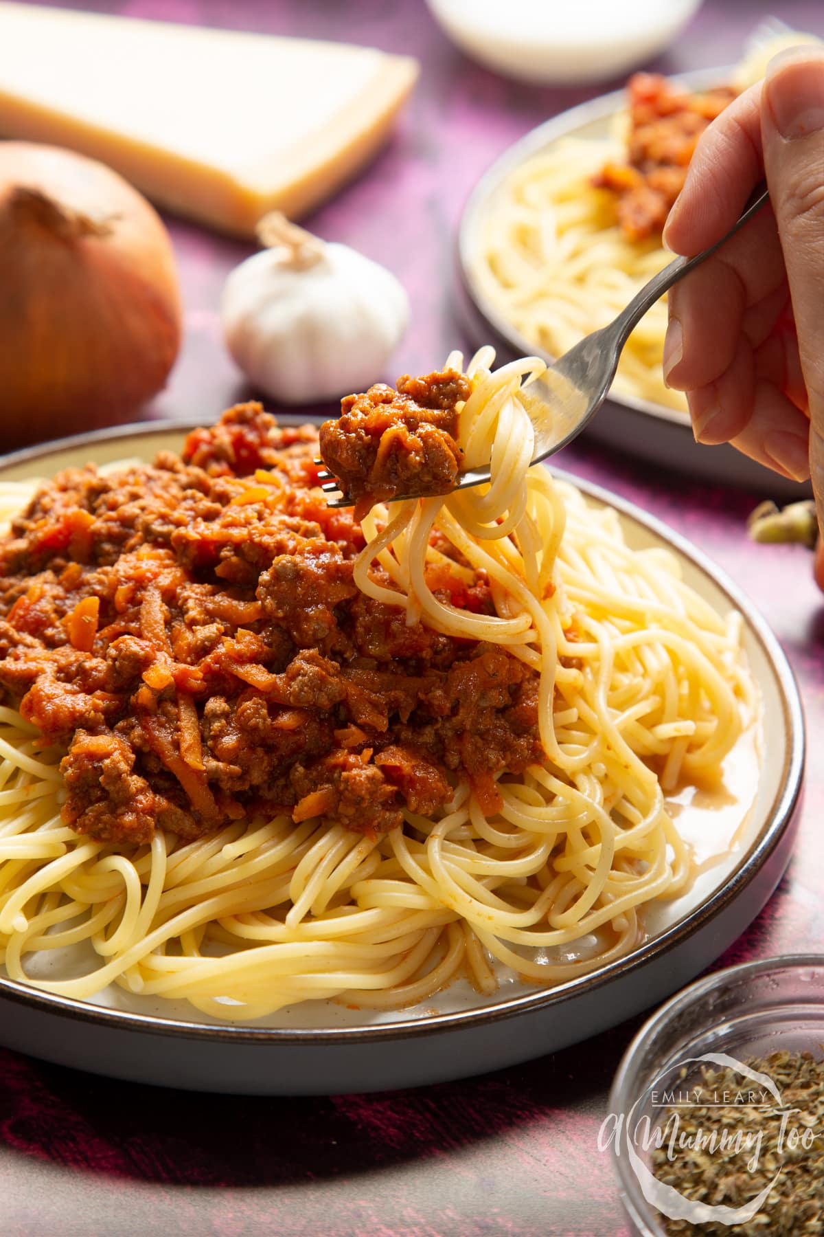 Side view of spaghetti bolognese Gordon Ramsay style served on plates. A fork lifts spaghetti from the plate.