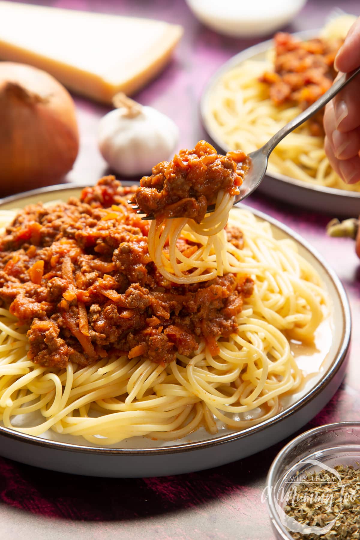 Side view of spaghetti bolognese Gordon Ramsay style served on plates. A hand holds a fork lifting spaghetti from the plate.