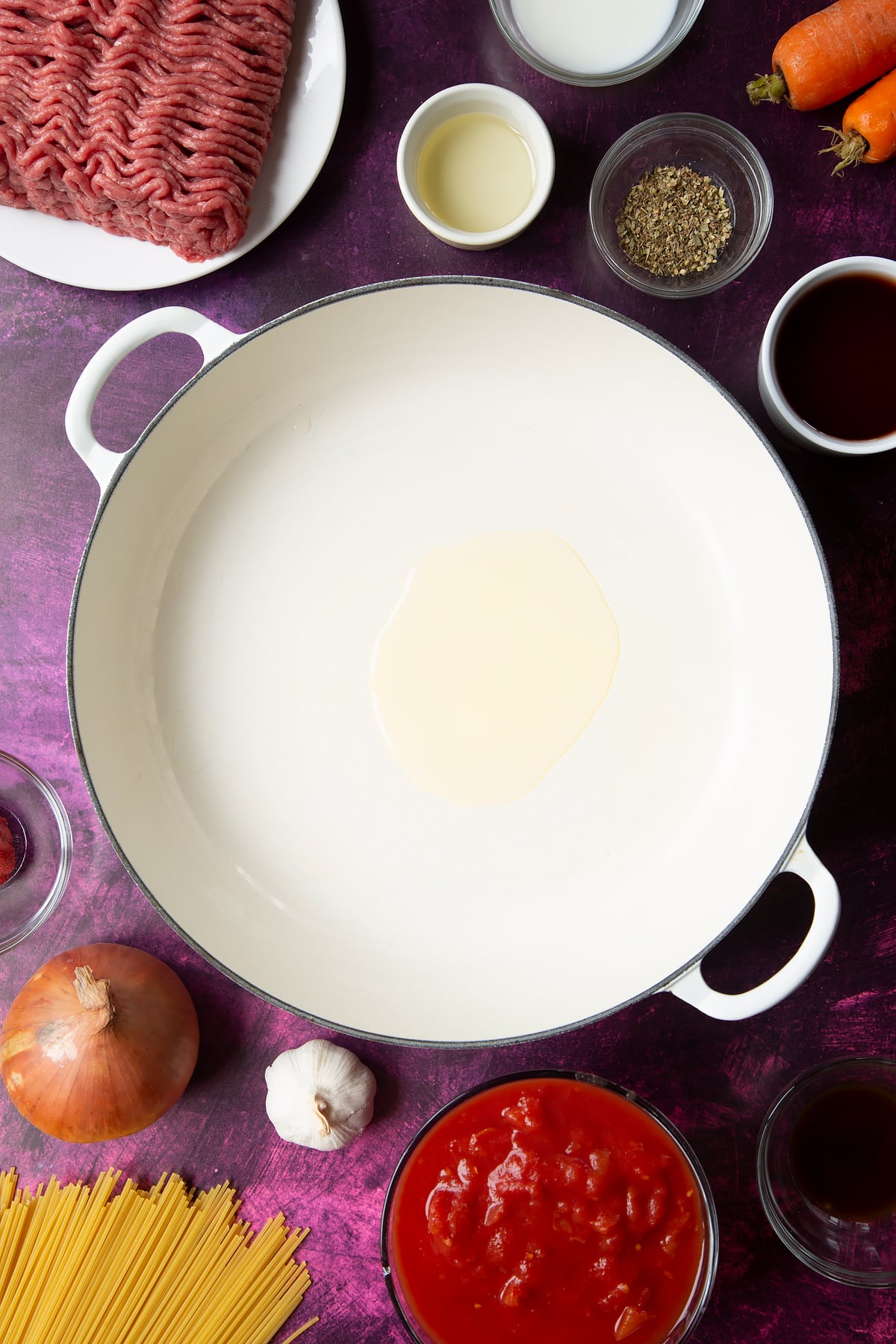 A large frying pan with olive oil. Ingredients to make spaghetti bolognese Gordon Ramsay style surround the pan.