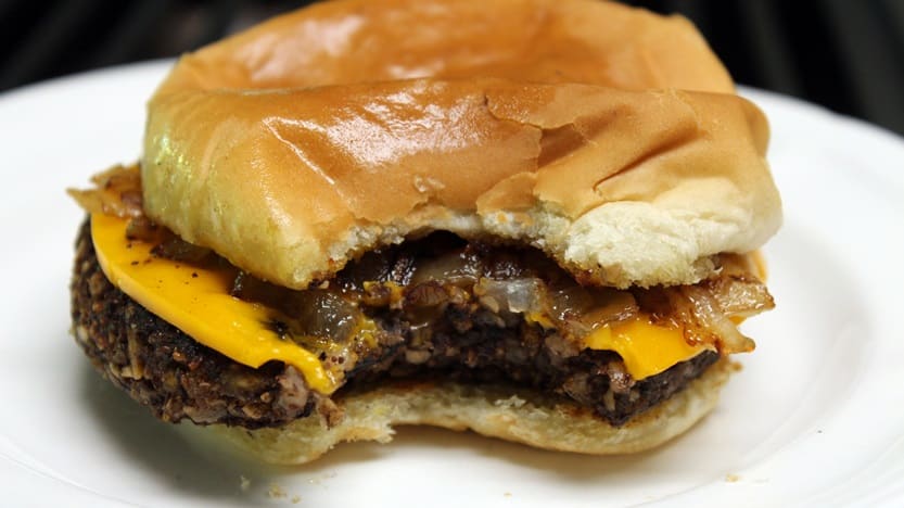 Vegan butter burger missing a bite out of the side. The burger is topped with cheese and onions and on a plain white plate.