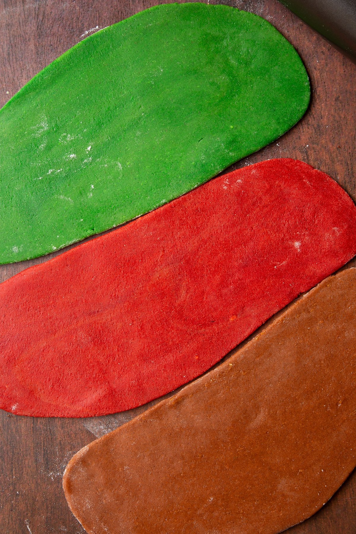 Red, green and brown cookie dough, rolled out side by side.