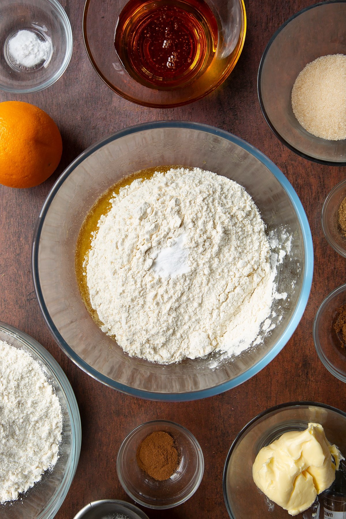 Melted butter, sugar and golden syrup topped with flour and bicarbonate of soda in a bowl. Ingredients to make autumn cookies surround the bowl.