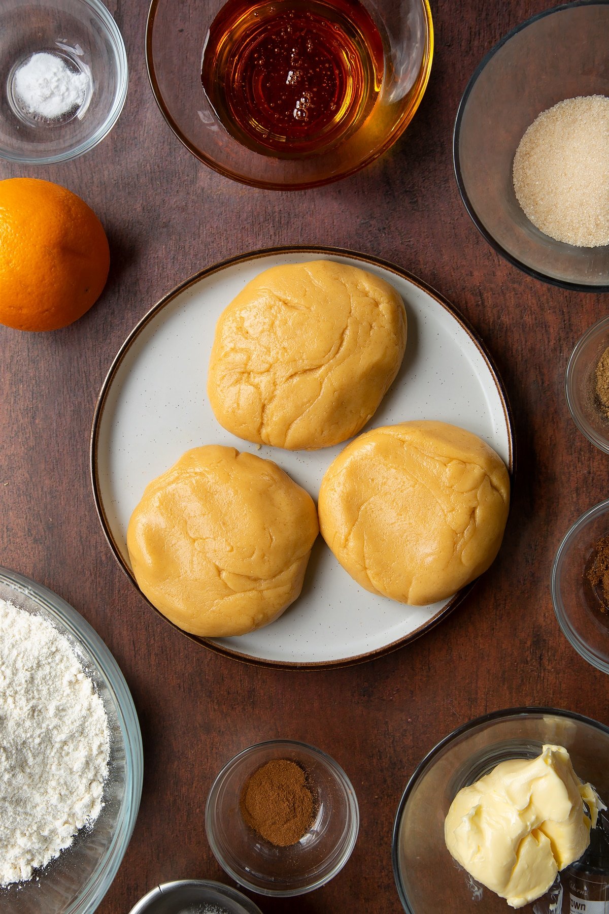 Three balls of cookie dough on a plate. Ingredients to make autumn cookies surround the plate.