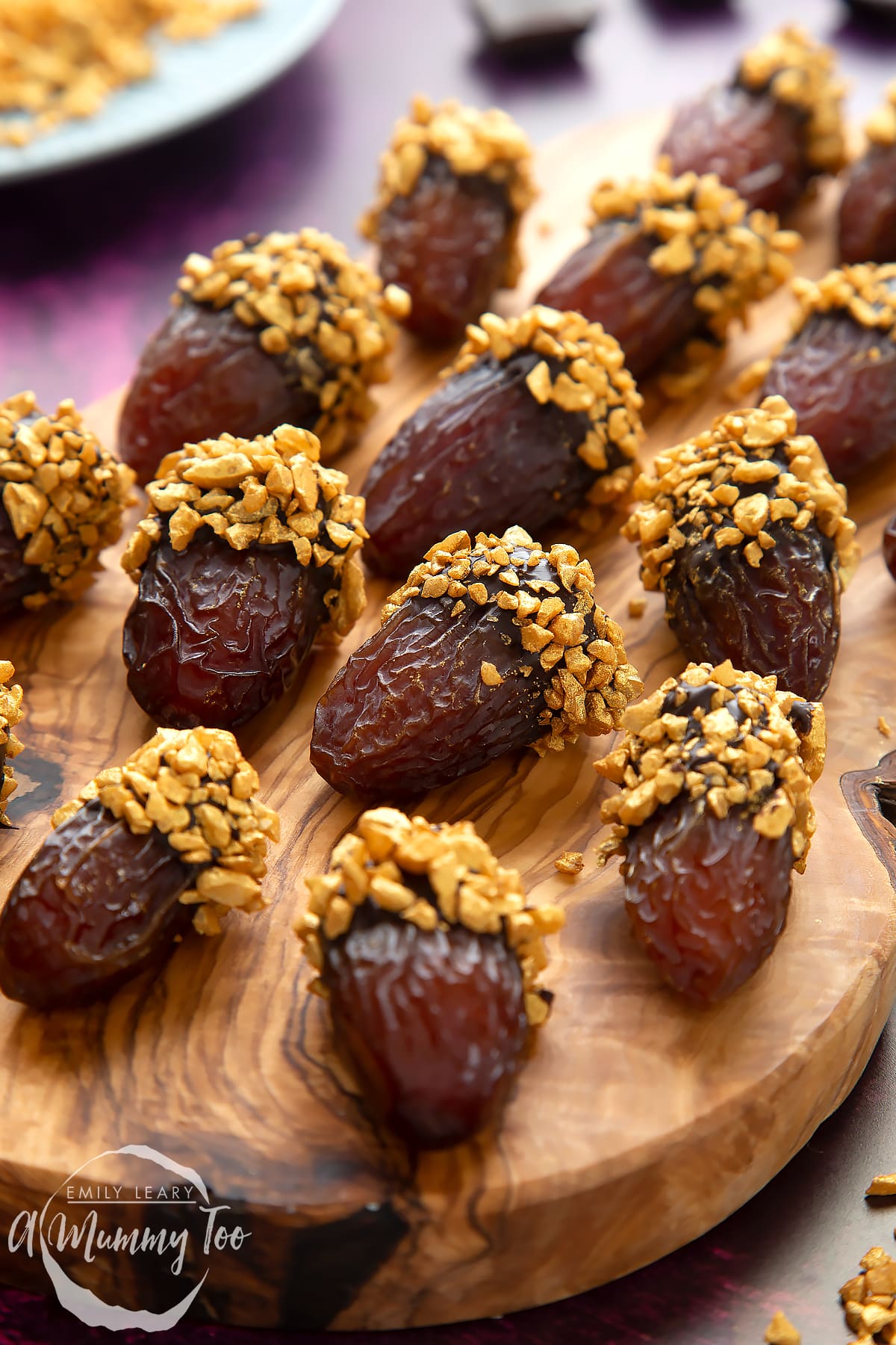 Medjool dates dipped in chocolate. The chocolate dates are on a wooden board and have be studded with gold chopped nuts.