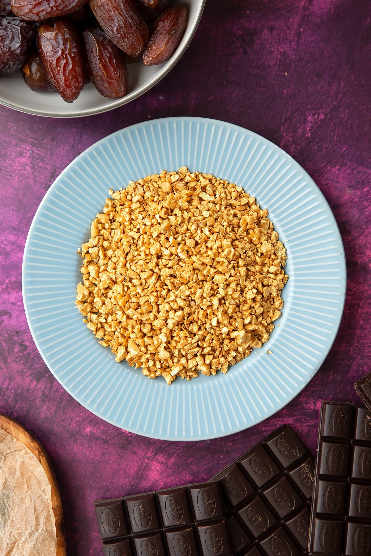 Chopped walnuts sprayed gold on a blue plate, surrounded by ingredients to make chocolate dates. 