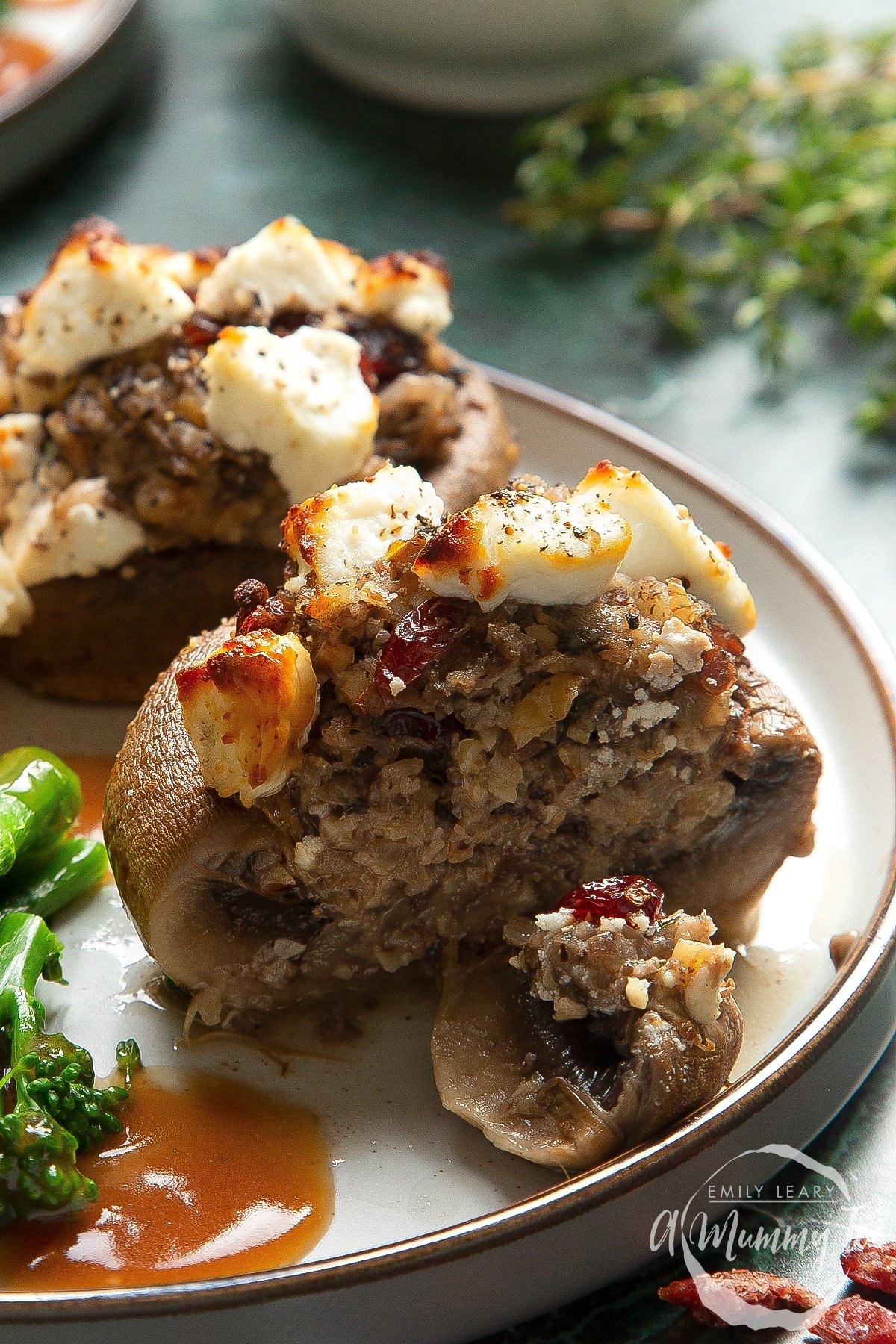 Front angle shot of halved Christmas stuffed mushrooms served on a white plate with a mummy too logo in the lower-right corner