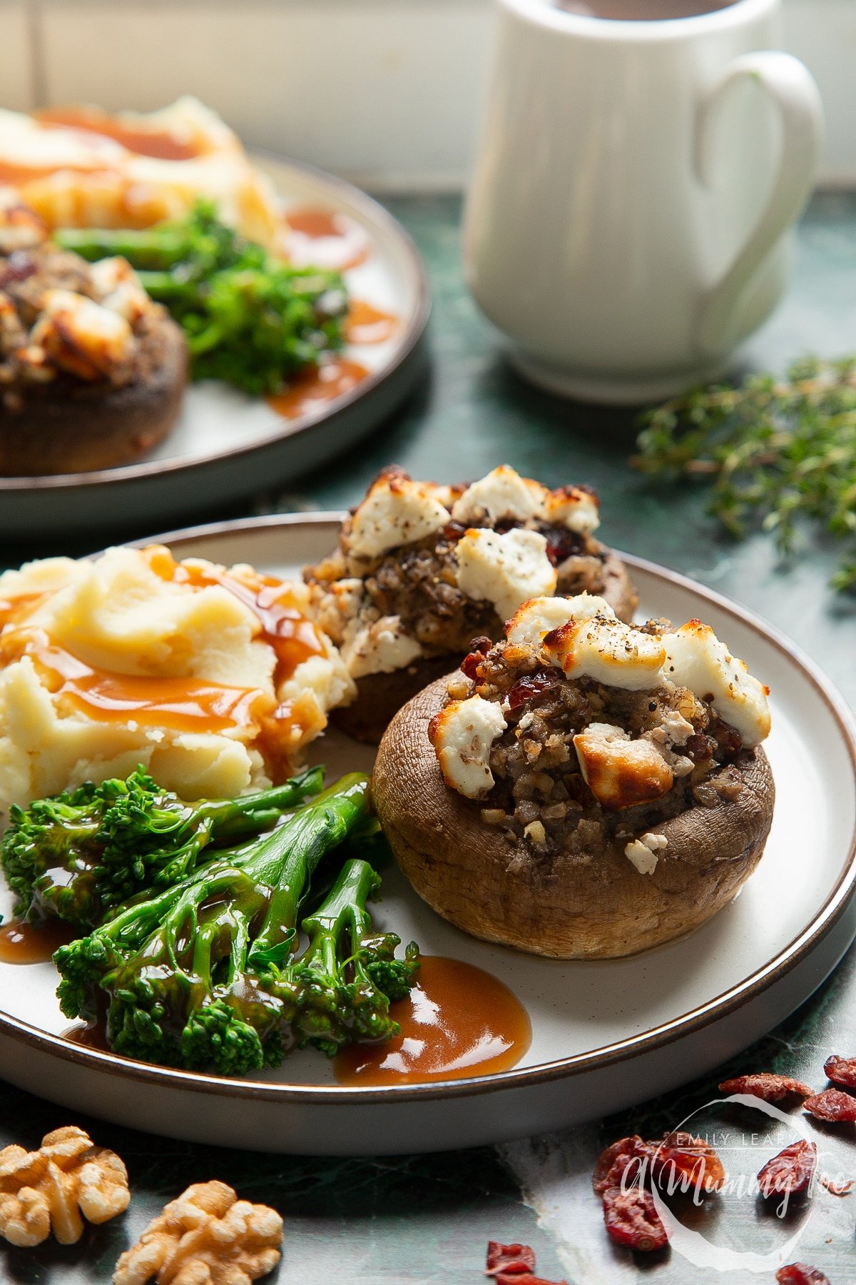 Front angle shot of Christmas stuffed mushrooms with mashed potato and vegetable on the side served on a white plate with a mummy too logo in the lower-right corner