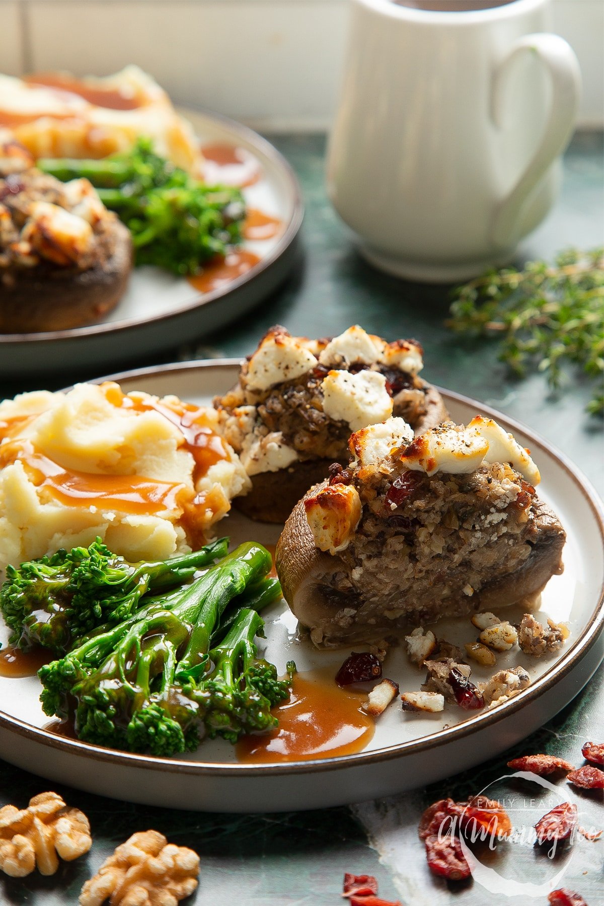 Front angle shot of stuffed mushrooms topped with creamy goat's cheese served on a gray plate with a mummy too logo in the lower-right corner