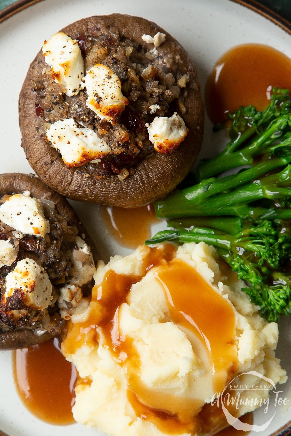 Overhead shot of a Festive Christmas stuffed mushroom with mashed potato and cauliflower on the side served on a white plate with a mummy too logo in the lower-right corner