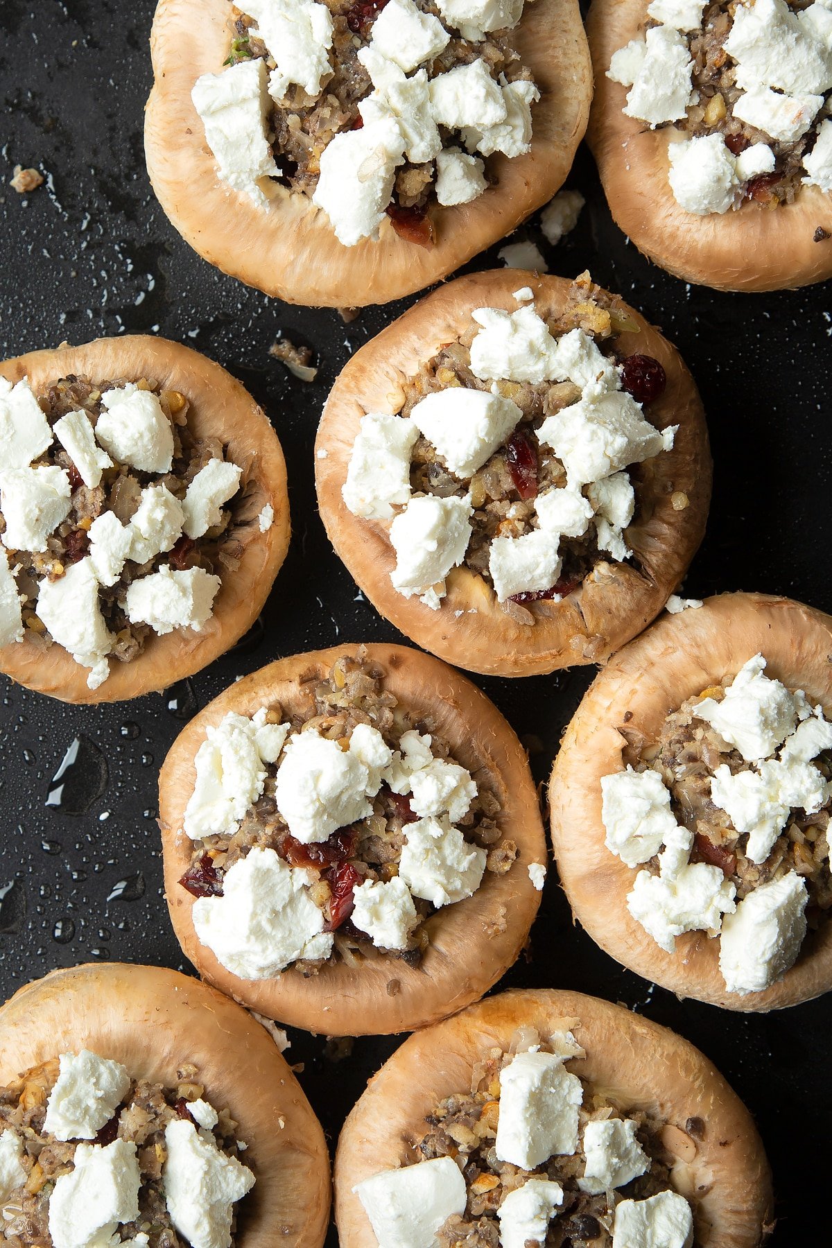 Overhead shot of filling inside mushrooms topped with goats cheese crumble on a baking tray 