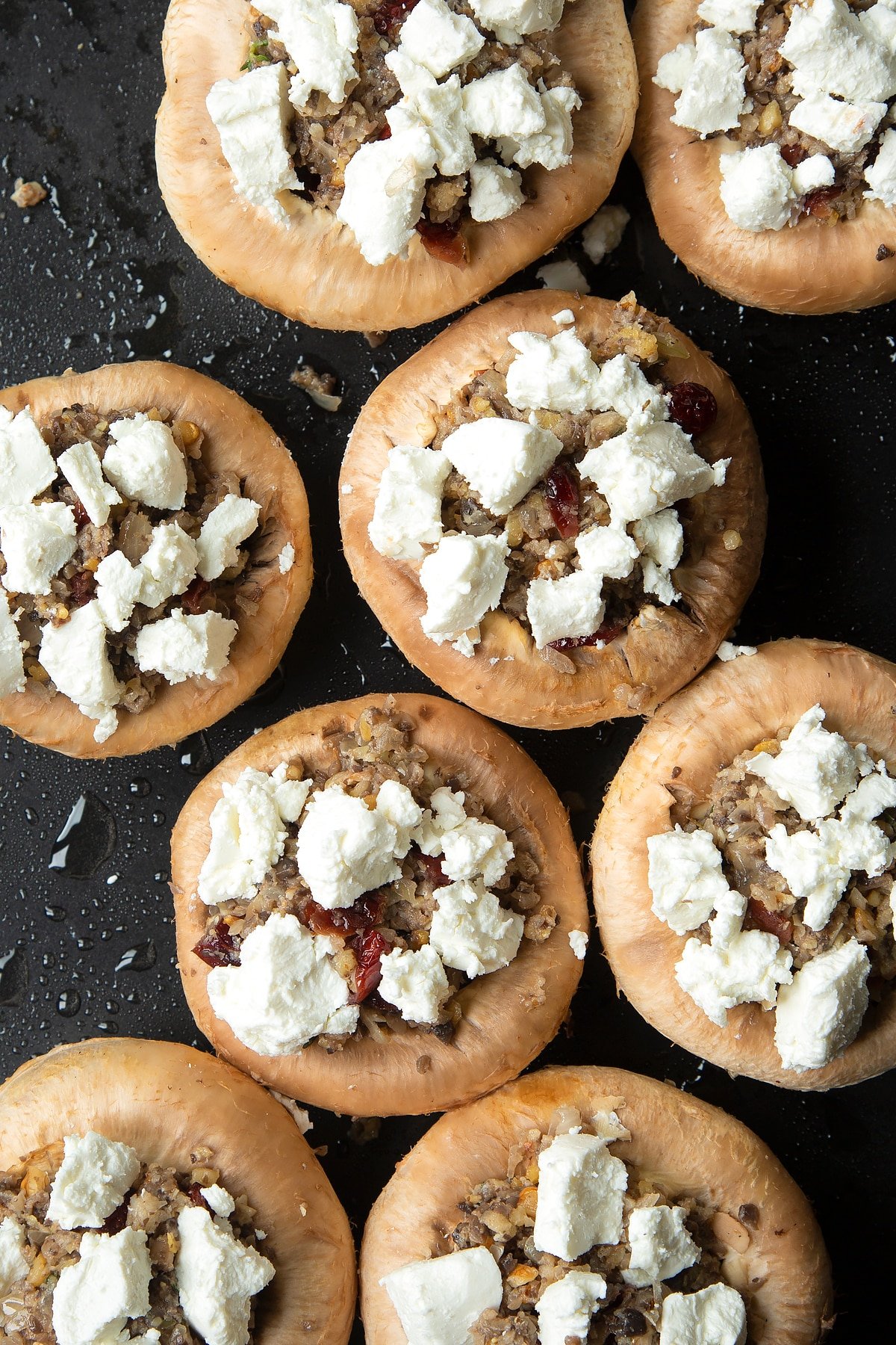Overhead shot of filling inside mushrooms topped with goats cheese crumble on a baking tray