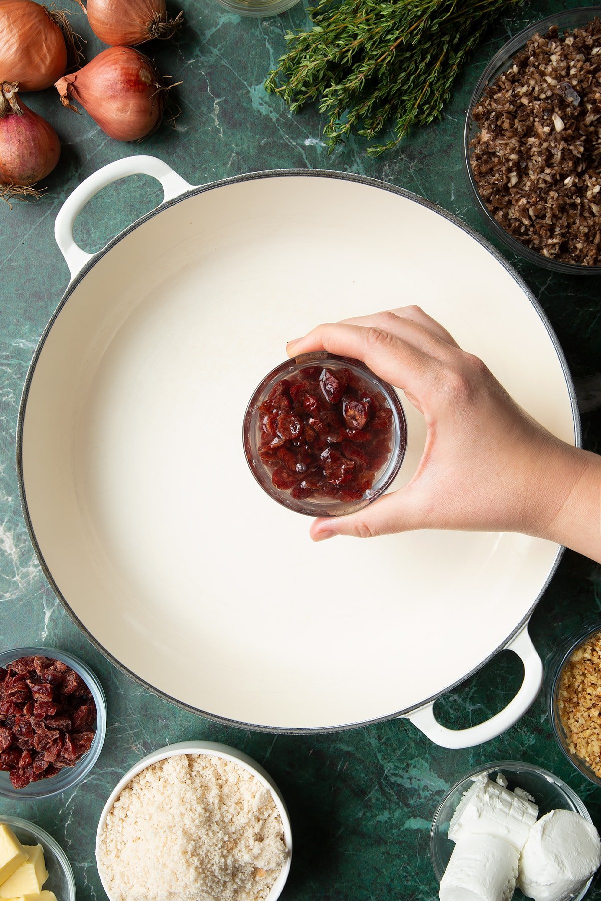 Overhead shot of a hand holding a bowl of cranberries above a large pan