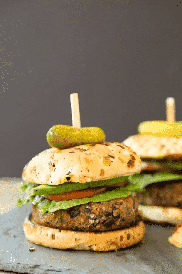 Butternut and chickpea burger with salad, topped with a pickle on a slate board. 