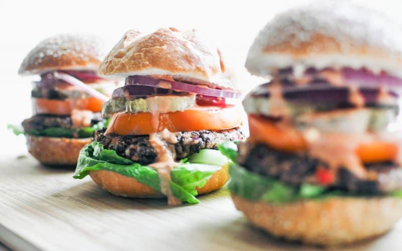 Three black bean burgers lined up on a wooden surface. The middle burger is the one most in focus.