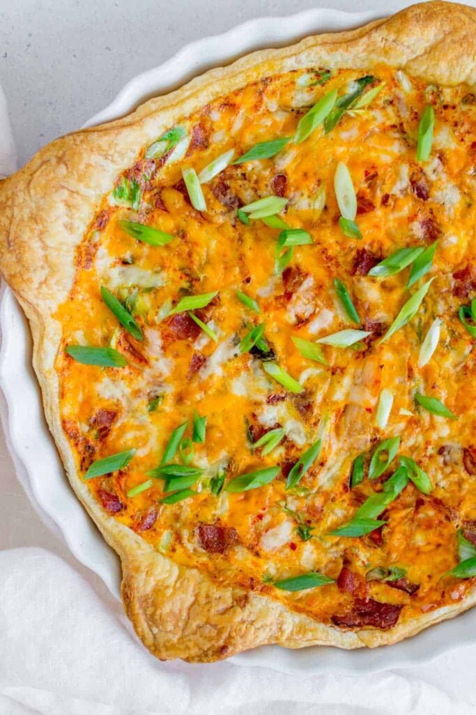 Puff pastry quiche in a white dish on a white speckled background. The image is close up so some of the quiche on the right hand side is cut off. 