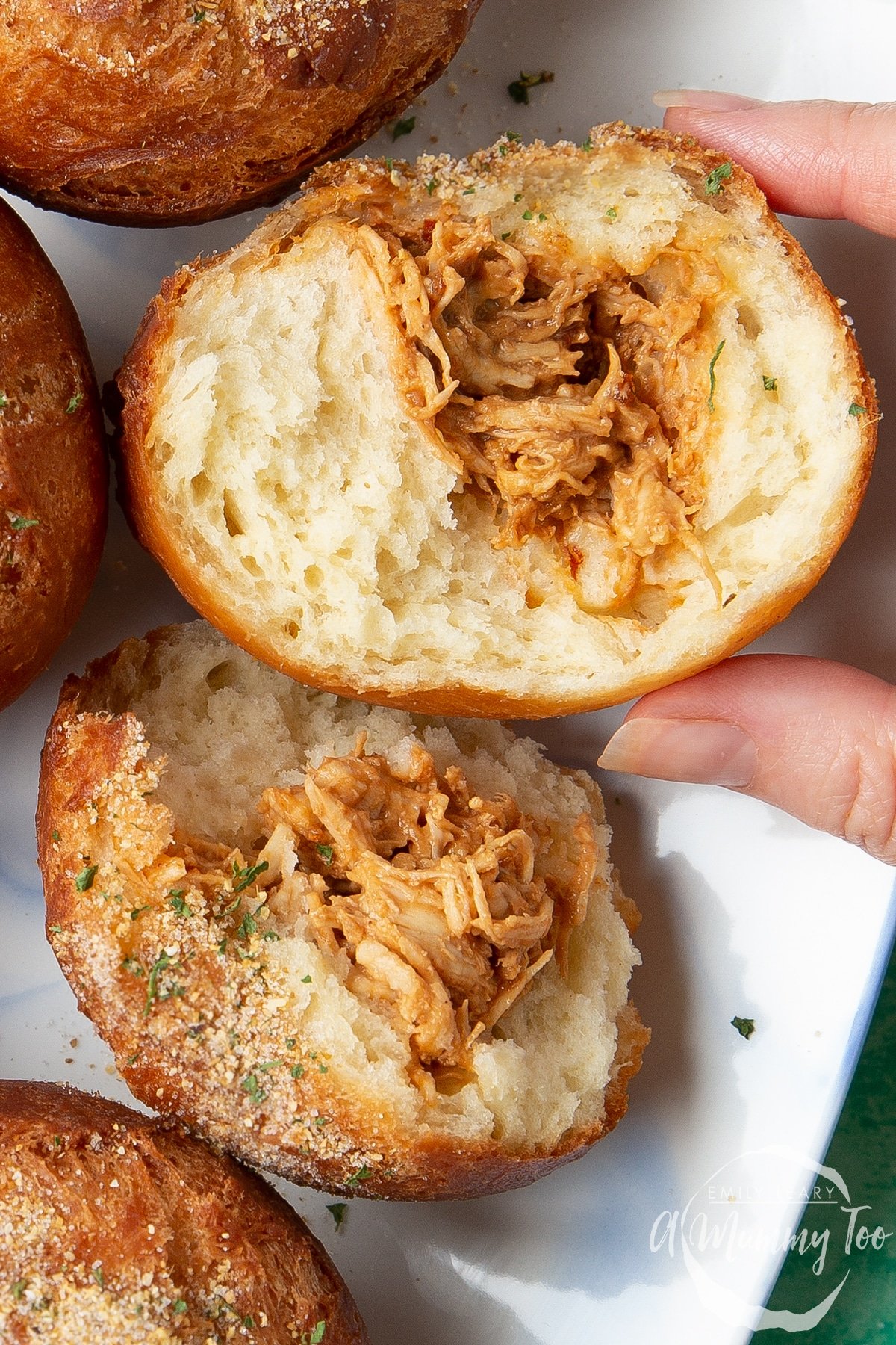 Close up of a torn open pulled chicken doughnut. A hand reaches for it.