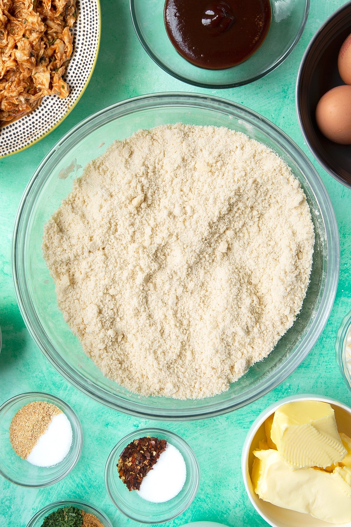 Flour and butter rubbed together in a glass mixing bowl. Ingredients to make chicken doughnuts surround the bowl.