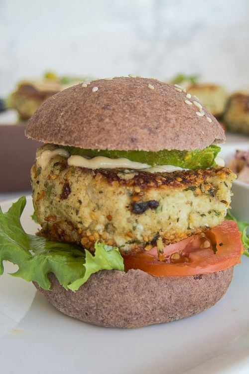 Keto cauliflower falafel burger on a white plate filled with lettuce and tomato.