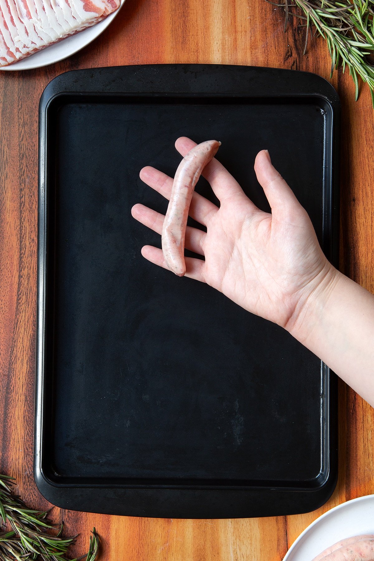 Overhead shot of a hand holding a sausage above black tray