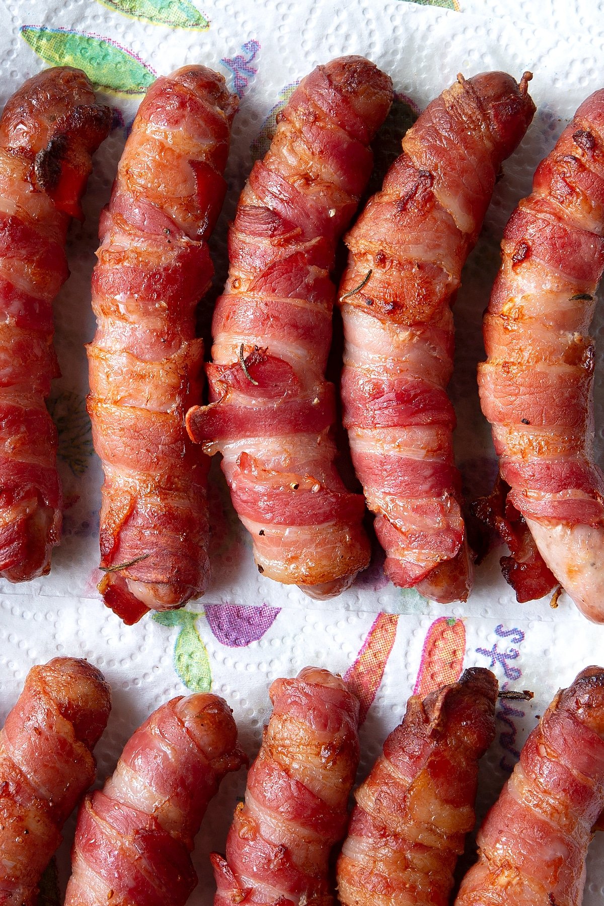 Close up overhead shot of the bacon wrapped sausages cooling on a paper towel.