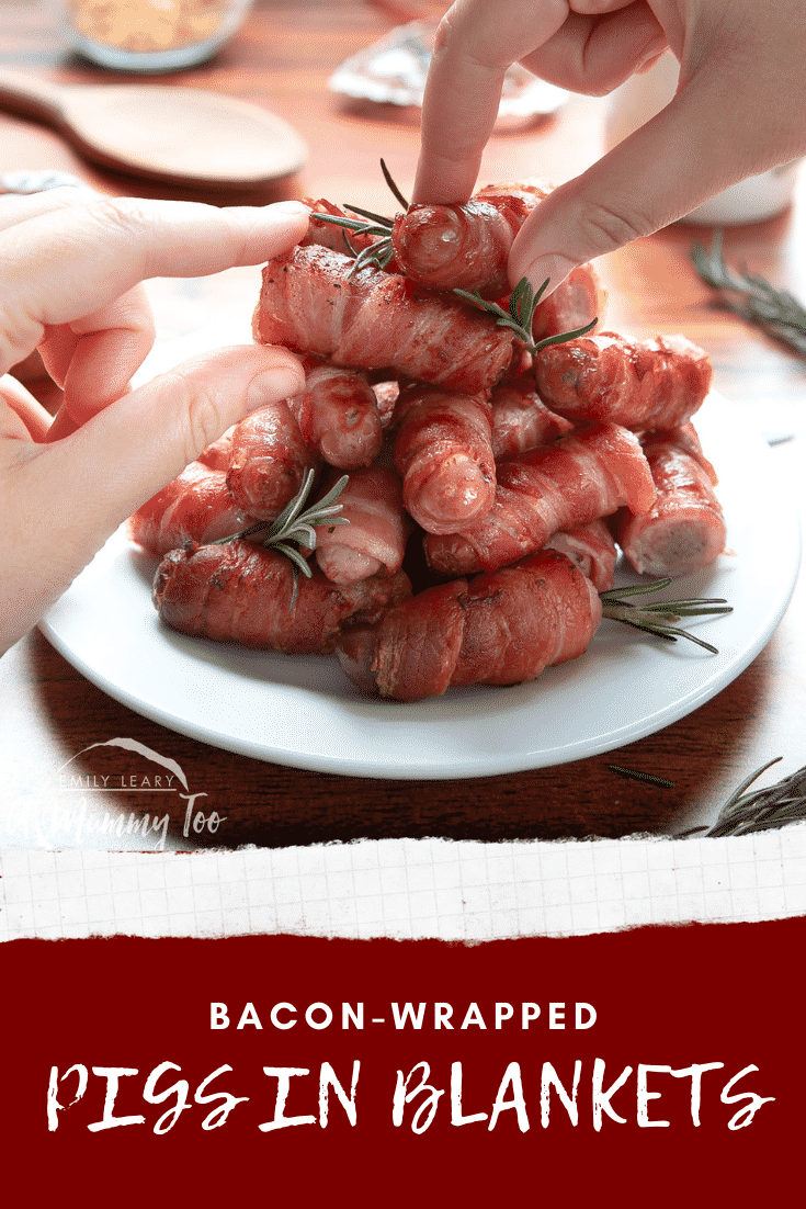 Forward shot showing two hands reaching in to grab one of the pigs in blankets on the stack which is set ontop of a white plate.