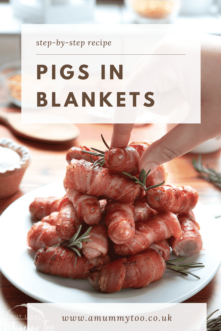 Front shot of a hand reaching in to grab a pig in blanket from the top of a stack build on a white plate. At the top of the image there's some text describing the image for Pinterest.