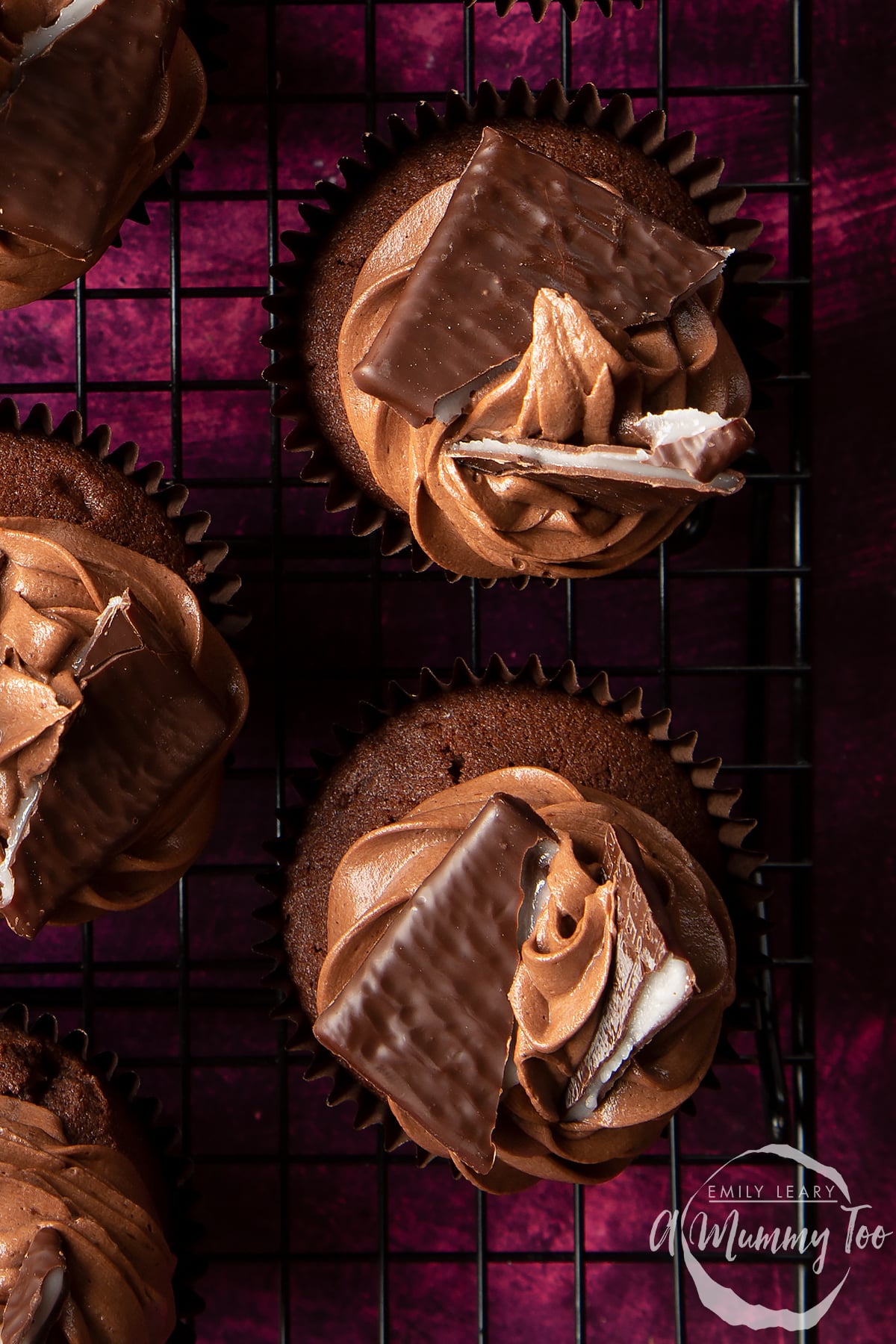 Close up on After Eight cupcakes cooling on a wire rack on a purple surface.