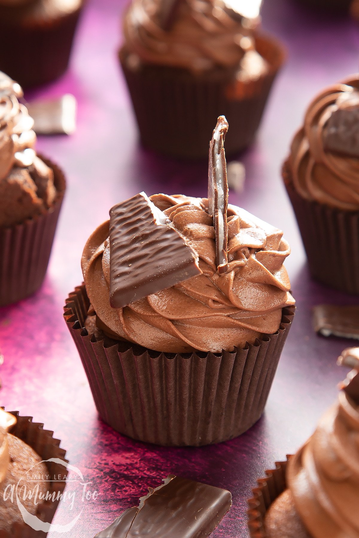 A close up of an After Eight cupcake on a purple surface. More cupcakes surround it.