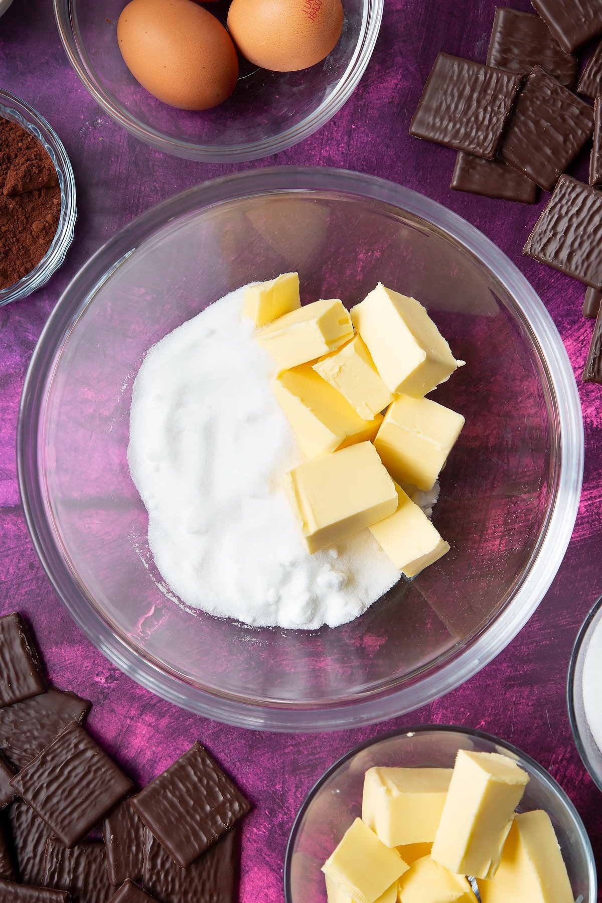 Sugar and butter in a glass mixing bowl. Ingredients to make After Eight cupcakes surround the bowl.