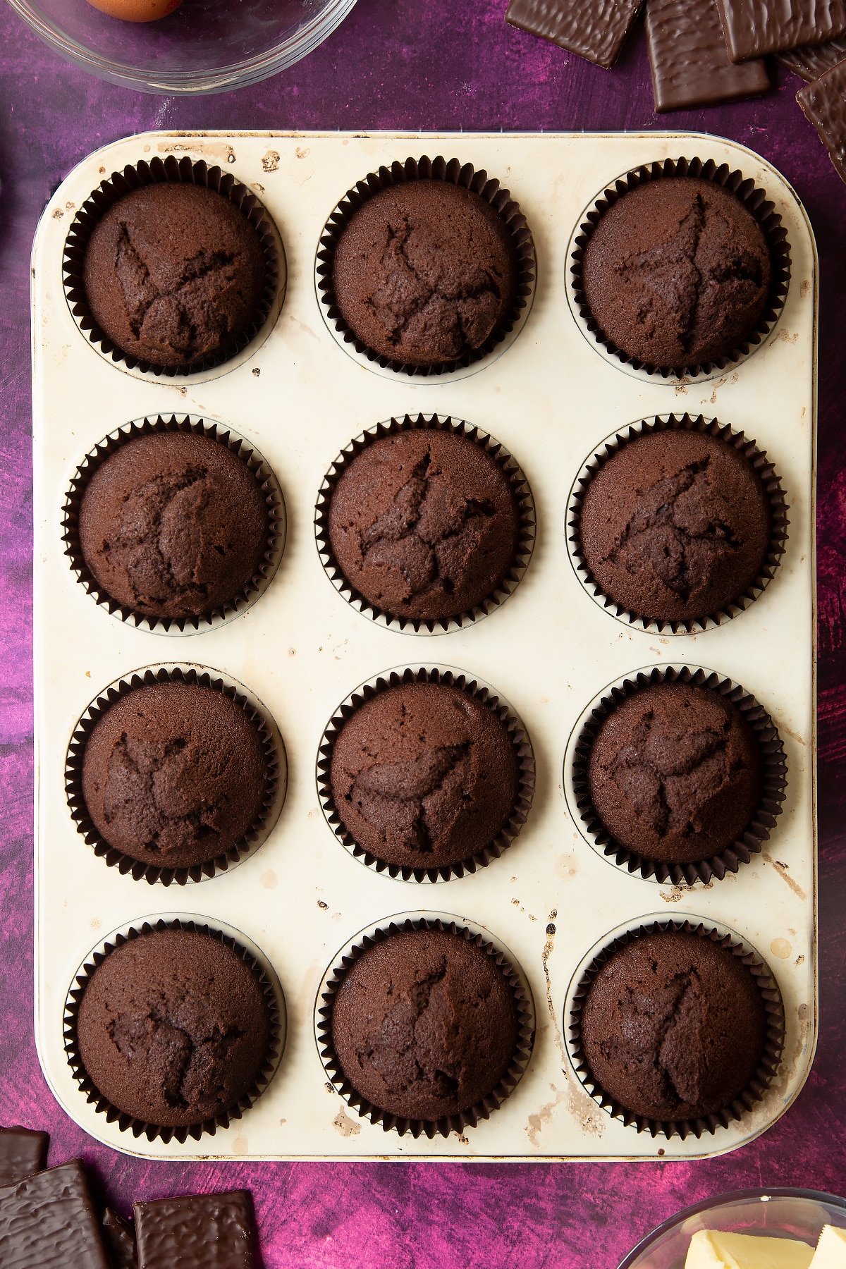 Baked chocolate cupcakes in a 12 hole muffin tray. Ingredients to make After Eight cupcakes surround the tray.