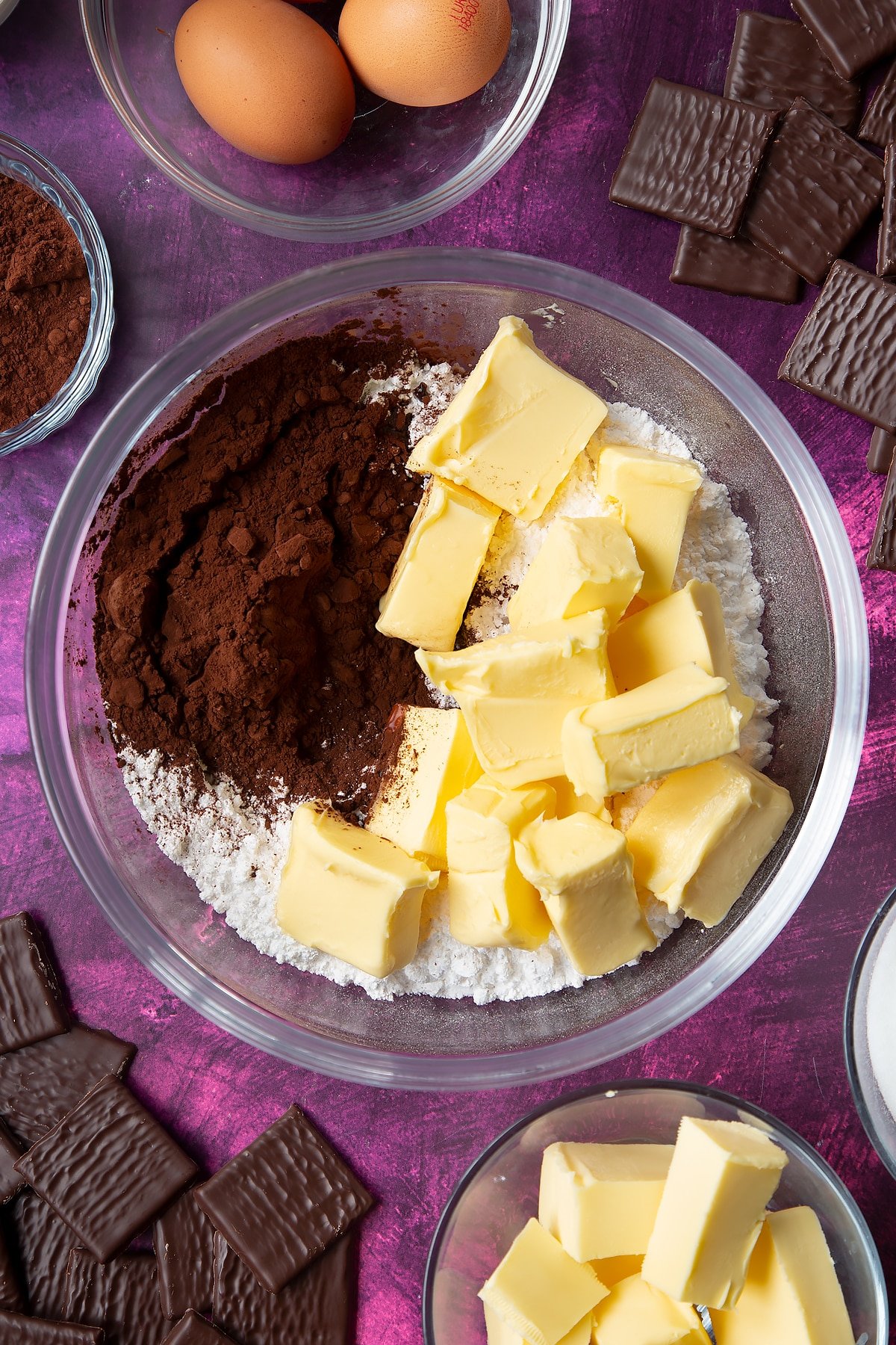 Icing sugar, butter and cocoa in a glass mixing bowl. Ingredients to make After Eight cupcakes surround the bowl.