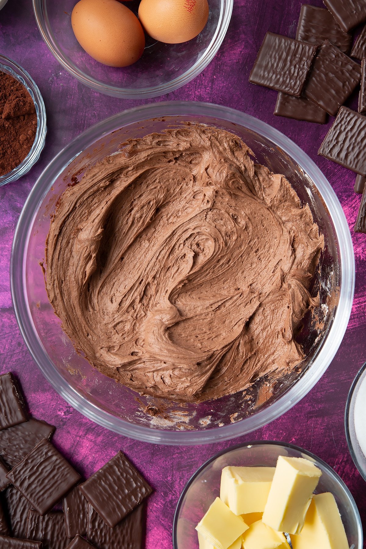 Chocolate buttercream in a glass mixing bowl. Ingredients to make After Eight cupcakes surround the bowl.