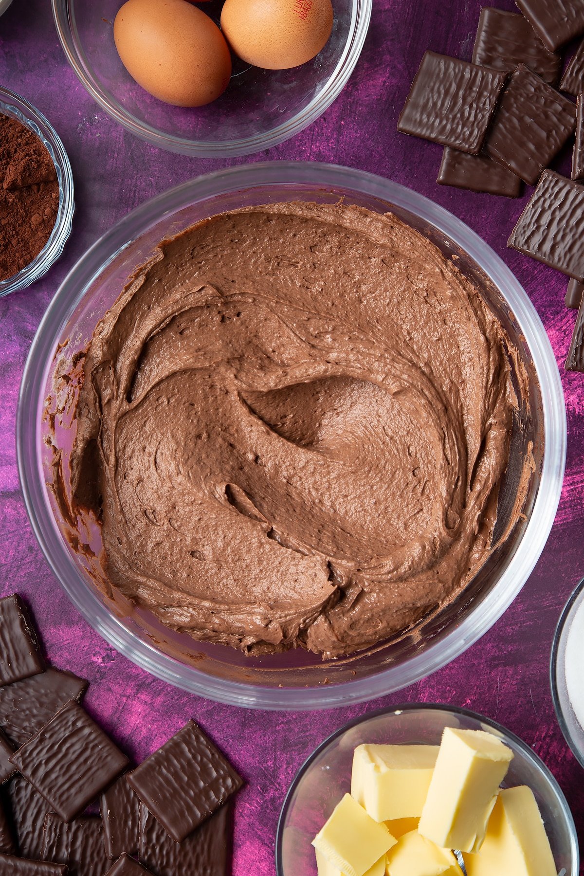 After Eight chocolate buttercream in a glass mixing bowl. Ingredients to make After Eight cupcakes surround the bowl.