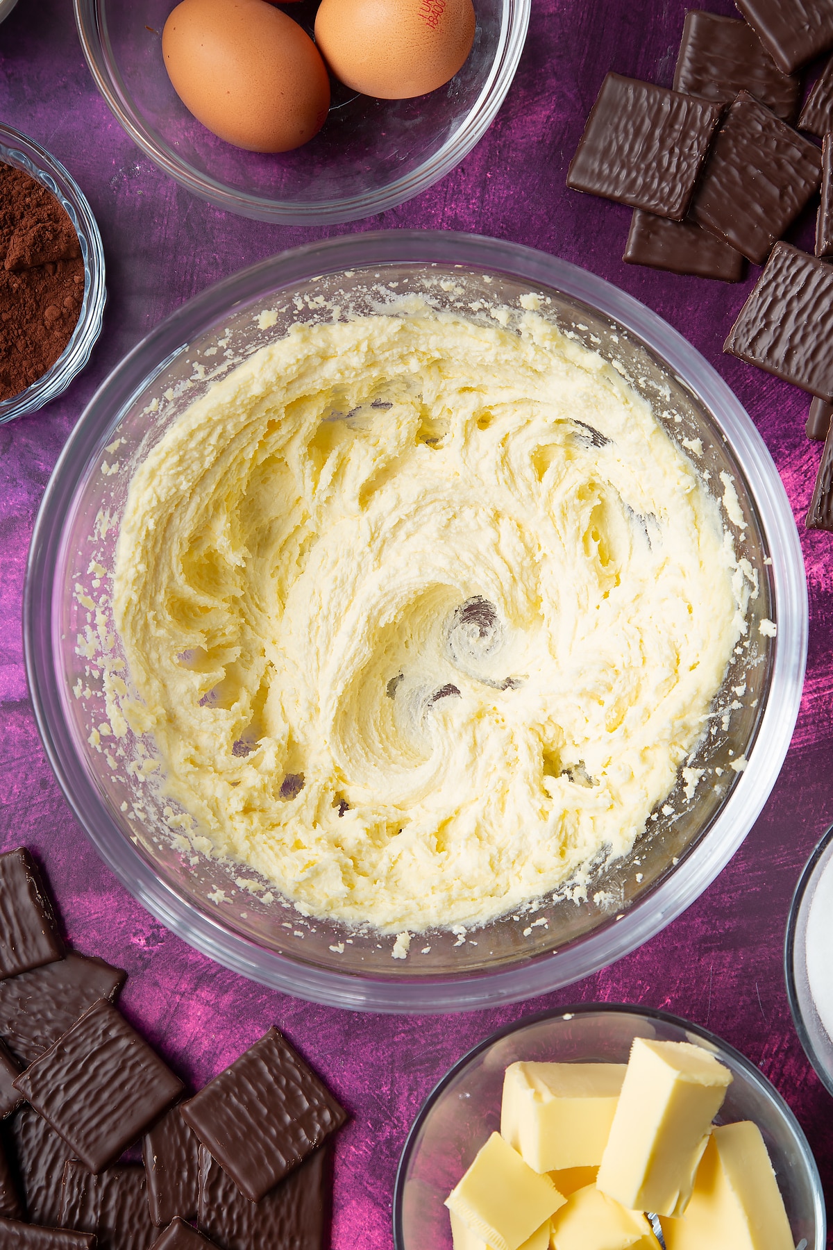 Sugar and butter beaten together in a glass mixing bowl. Ingredients to make After Eight cupcakes surround the bowl.