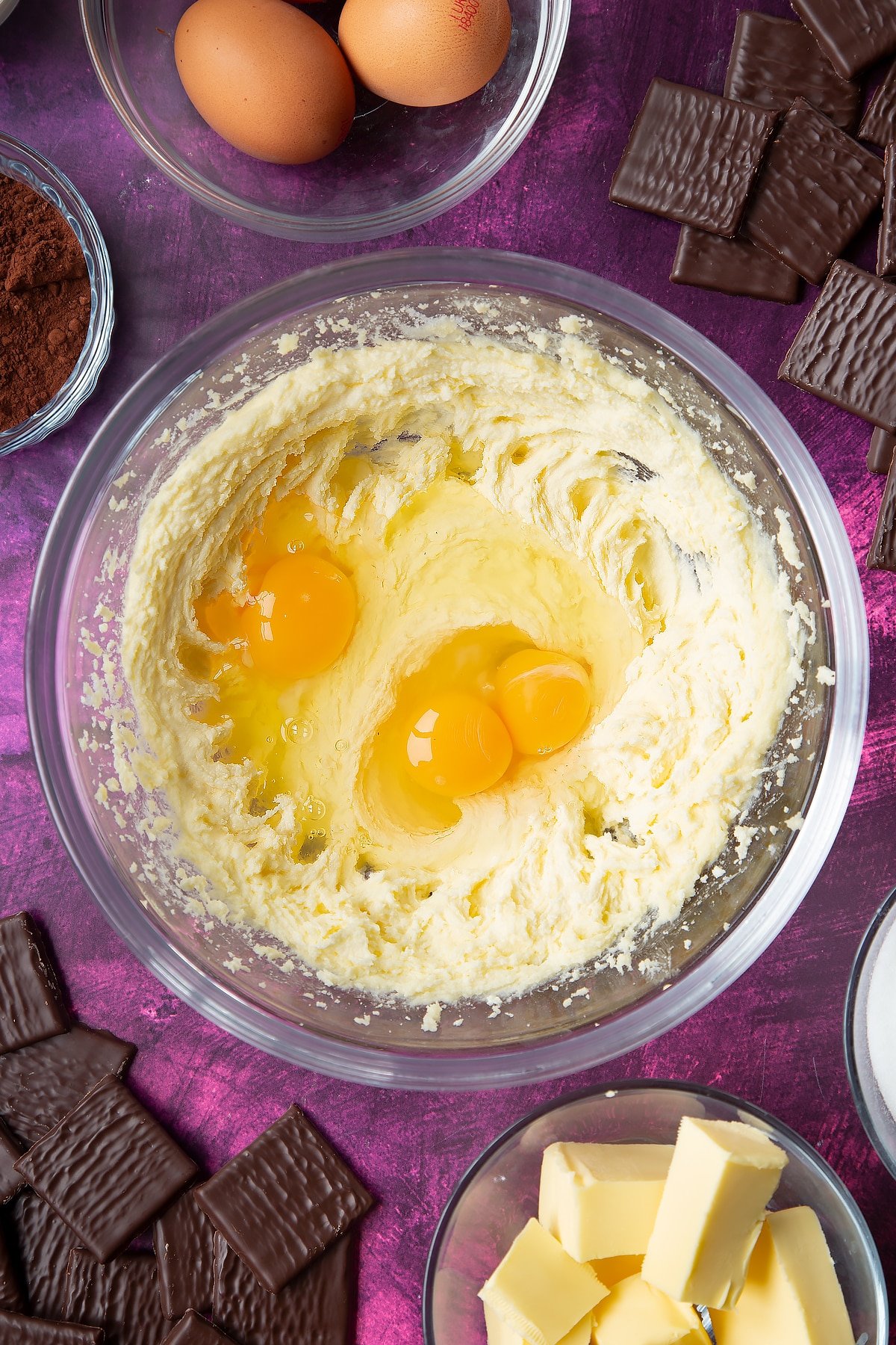 Sugar and butter beaten together in a glass mixing bowl with eggs on top. Ingredients to make After Eight cupcakes surround the bowl.