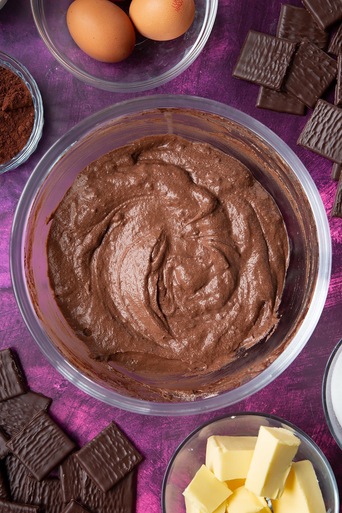 Chocolate cake batter in a glass mixing bowl. Ingredients to make After Eight cupcakes surround the bowl.