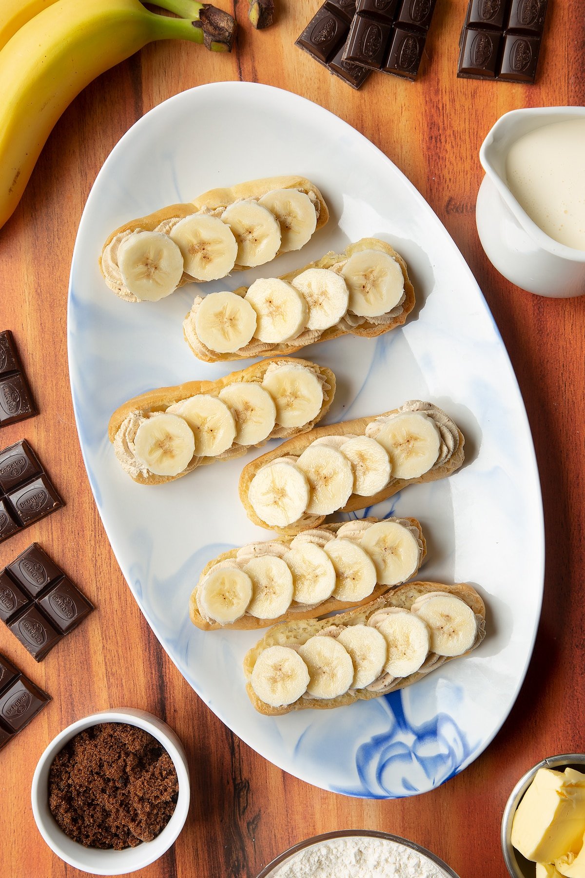 Overhead shot of eclair halves with slices of fresh banana on top served on a white plate