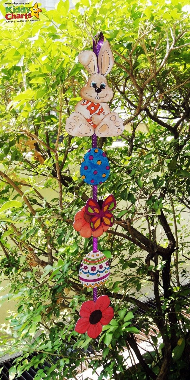 Coloured Easter images such as eggs, flowers and bunnies, cut up and strung on ribbon, hanging from a tree.