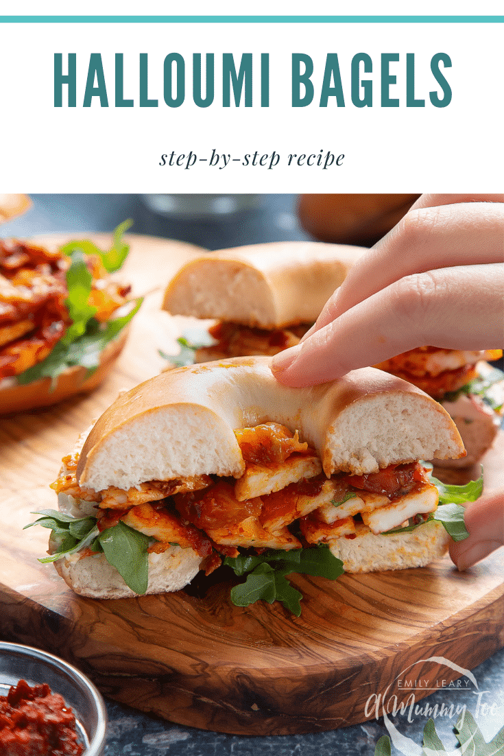 Two halloumi bagels on a wooden board. One is cut in half and a hand reaches for it. Caption reads: halloumi bagels step-by-step recipe