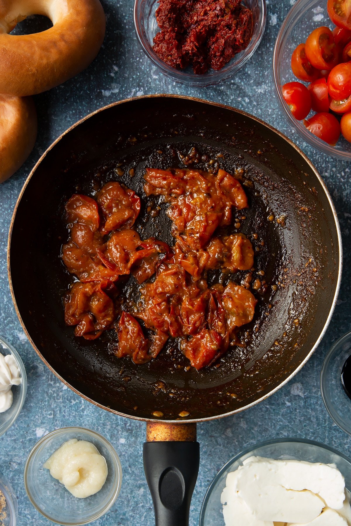 Cherry tomato salsa in a frying pan. Ingredients to make halloumi bagels surround the pan.