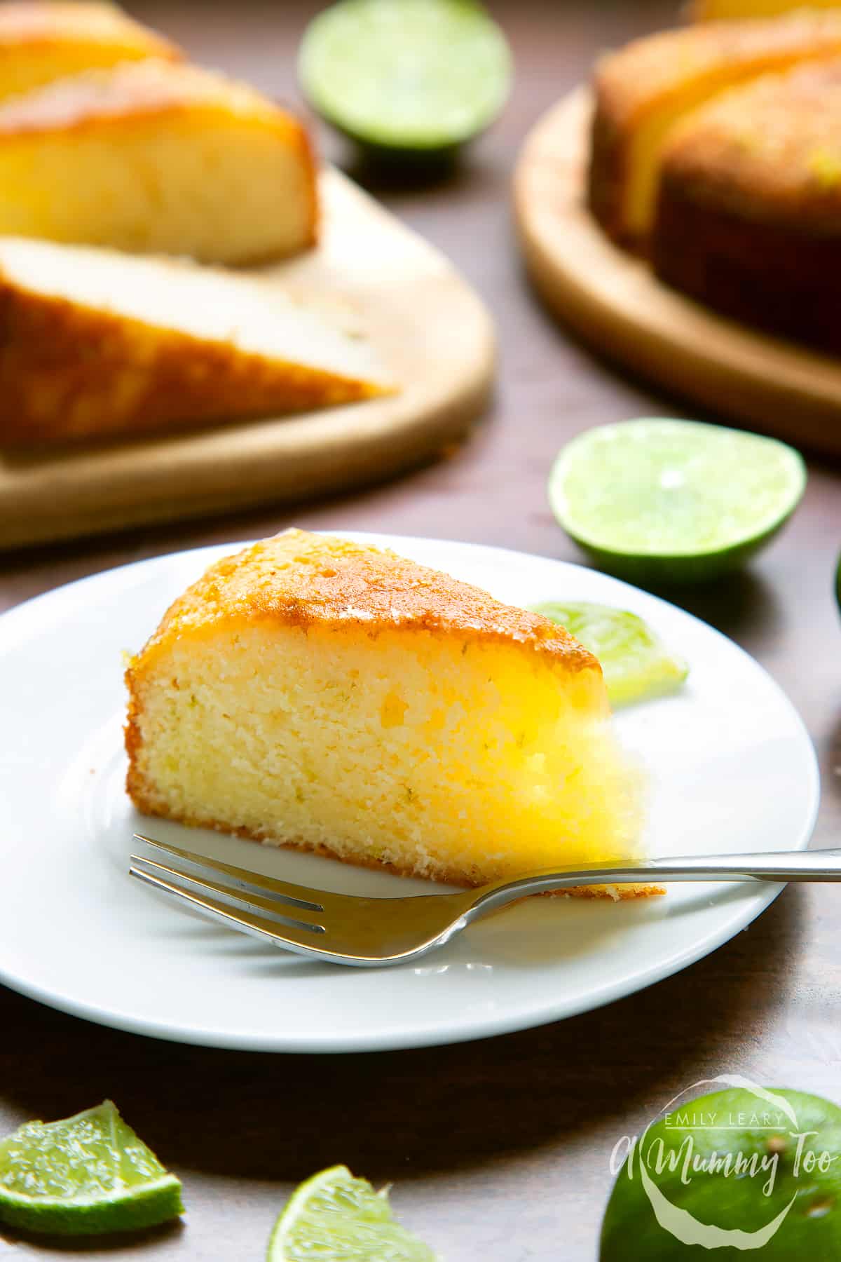 Slice of lime drizzle cake standing on a white plate with a fork.