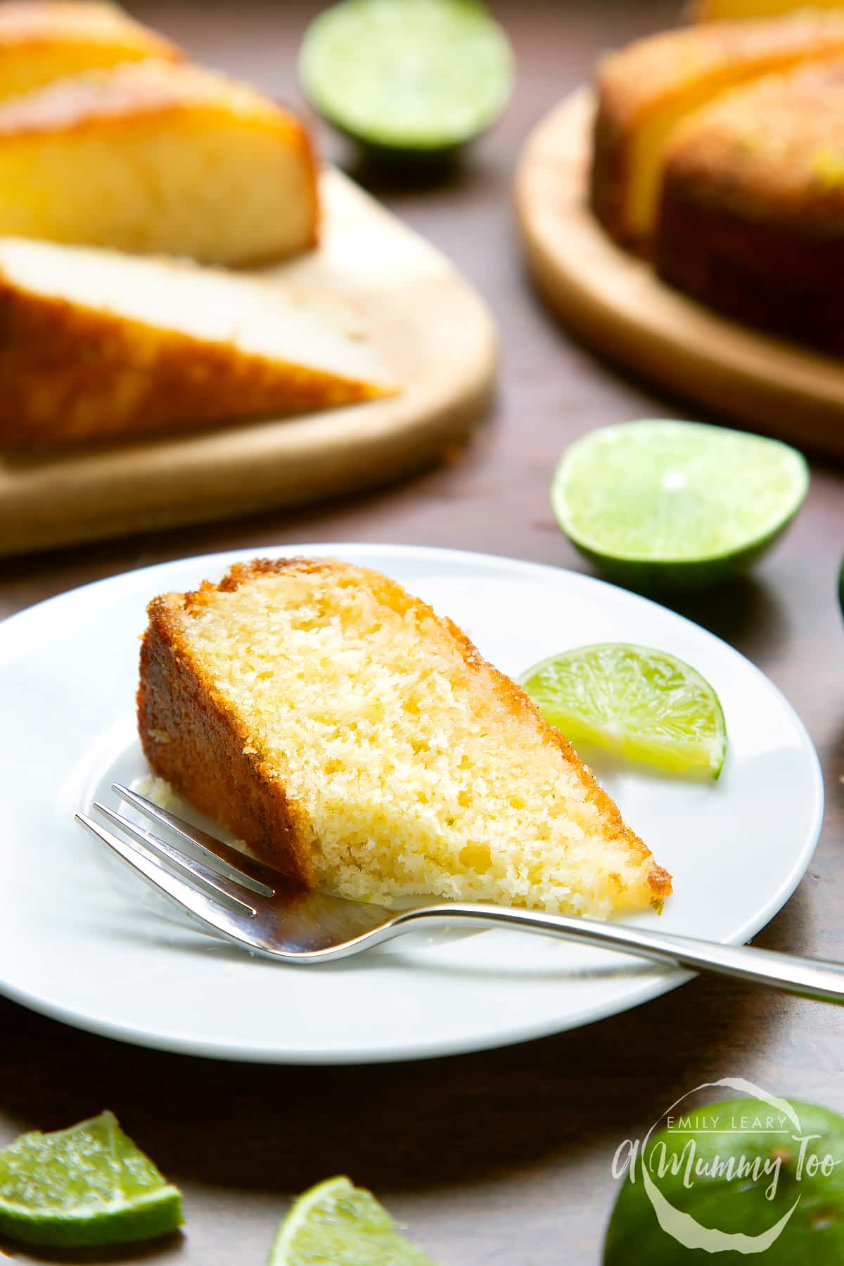 Slice of lime drizzle cake laying on a white plate with a fork. A piece has been eaten.