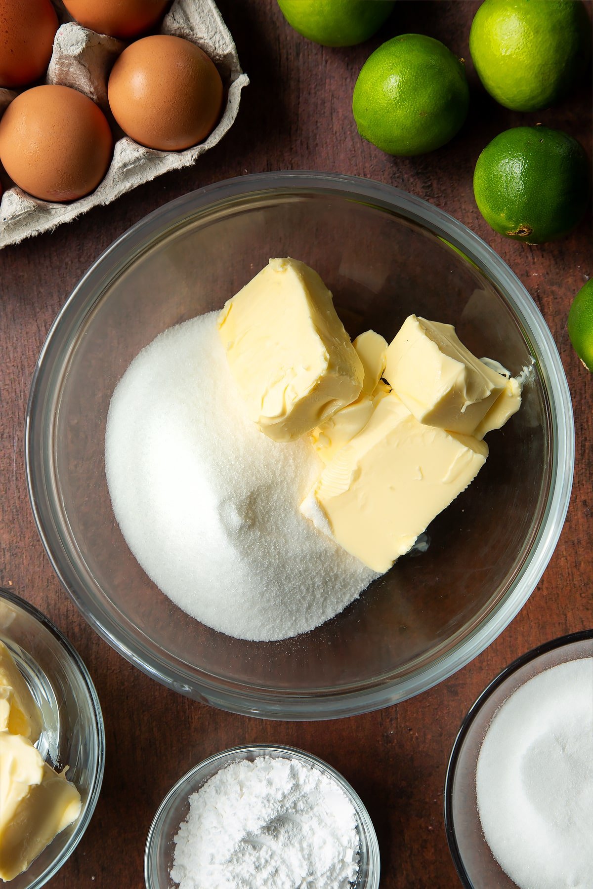 Butter and sugar in a mixing bowl. Ingredients to make lime drizzle cake surround the bowl.