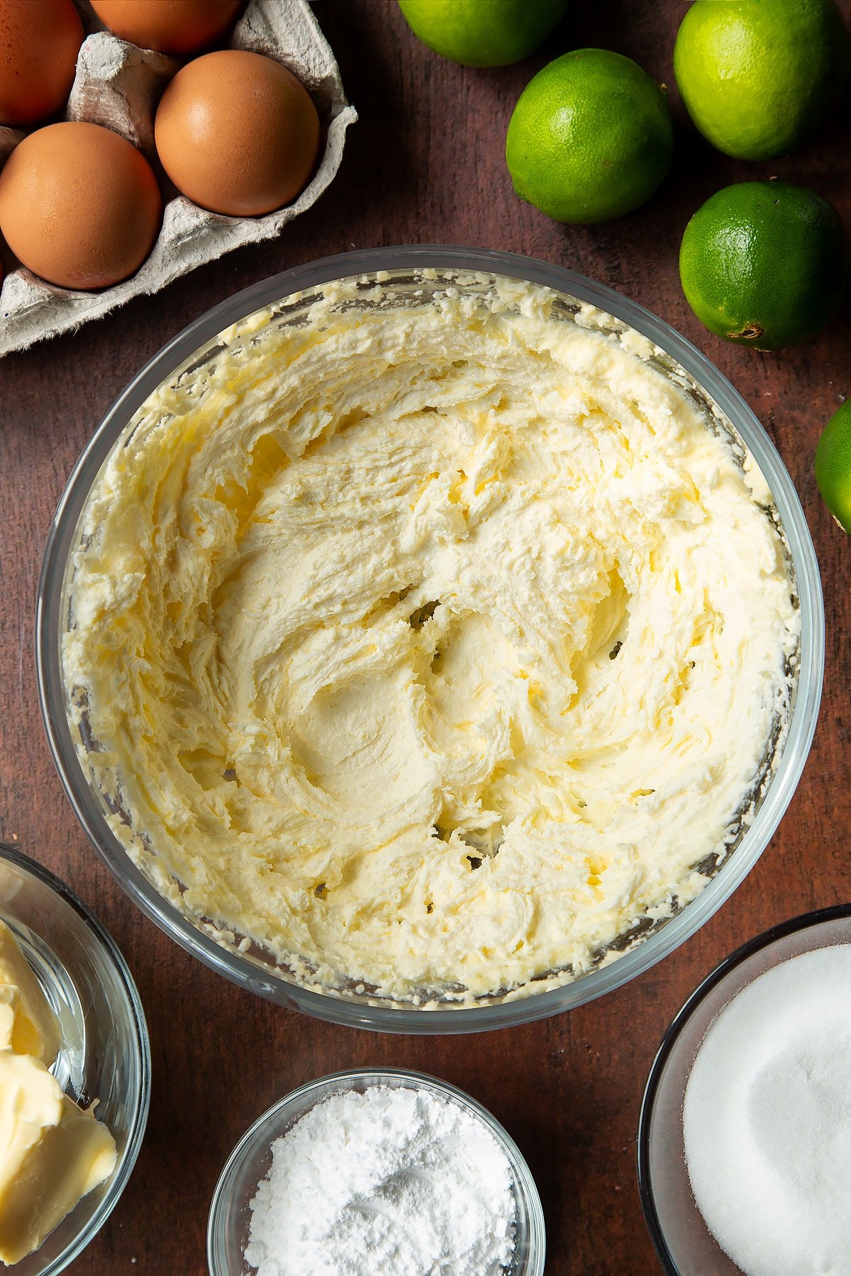 Butter and sugar beaten together in a mixing bowl. Ingredients to make lime drizzle cake surround the bowl.