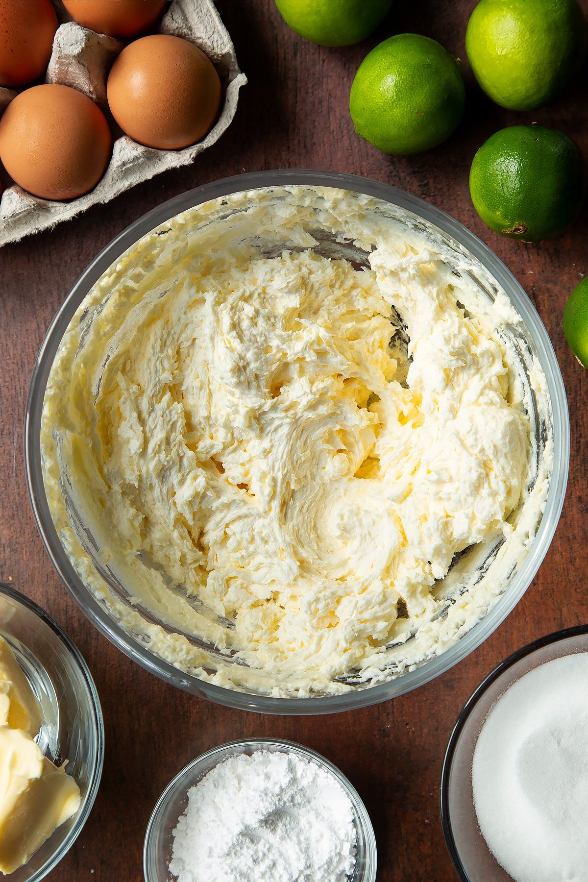Butter, sugar and eggs beaten together in a mixing bowl. Ingredients to make lime drizzle cake surround the bowl.