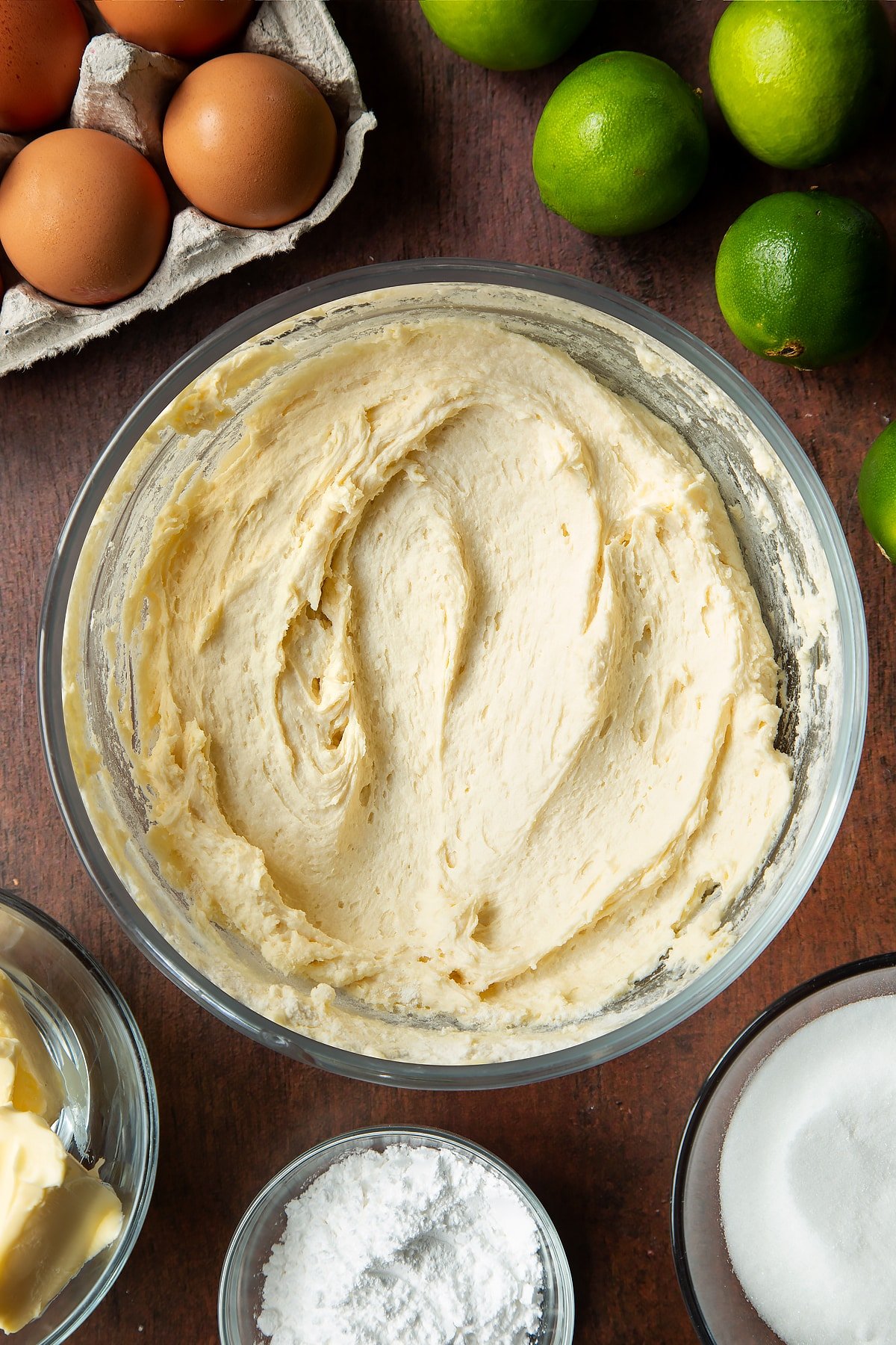 Basic cake batter in a mixing bowl. Ingredients to make lime drizzle cake surround the bowl.